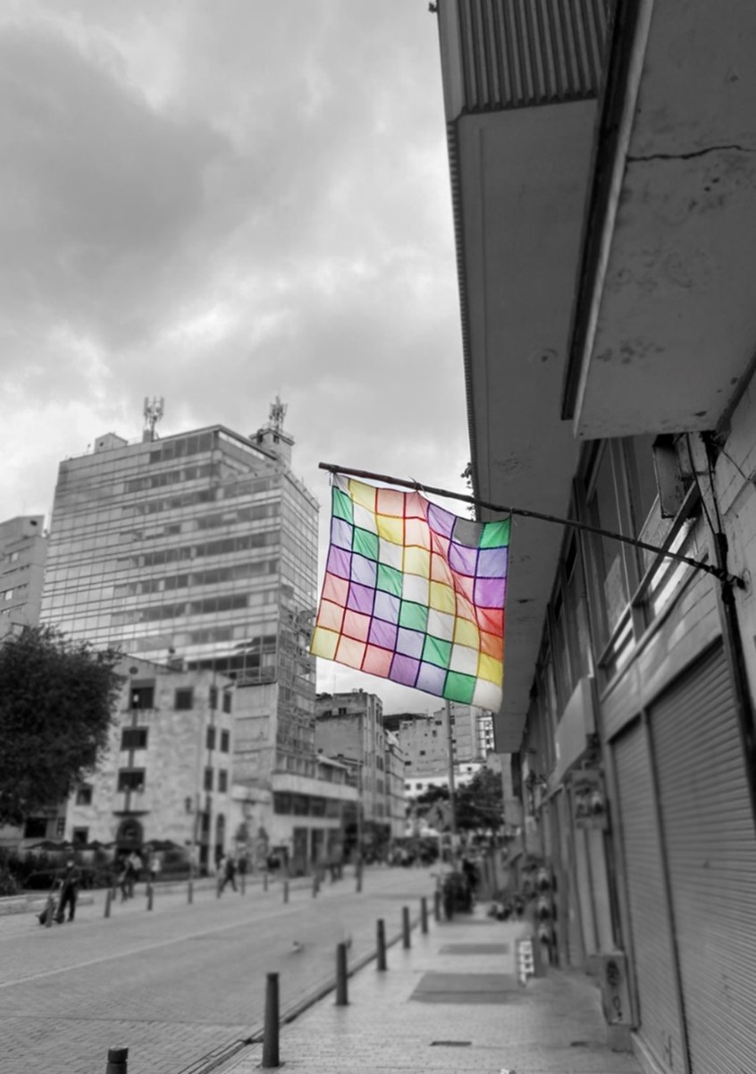 Wiphala en color izada en una calle de Bogotá con fodo blanco y negro. Imagen aportada por Alejandra Garrido Moreno integrante del  equipo de Revista Polisemia.